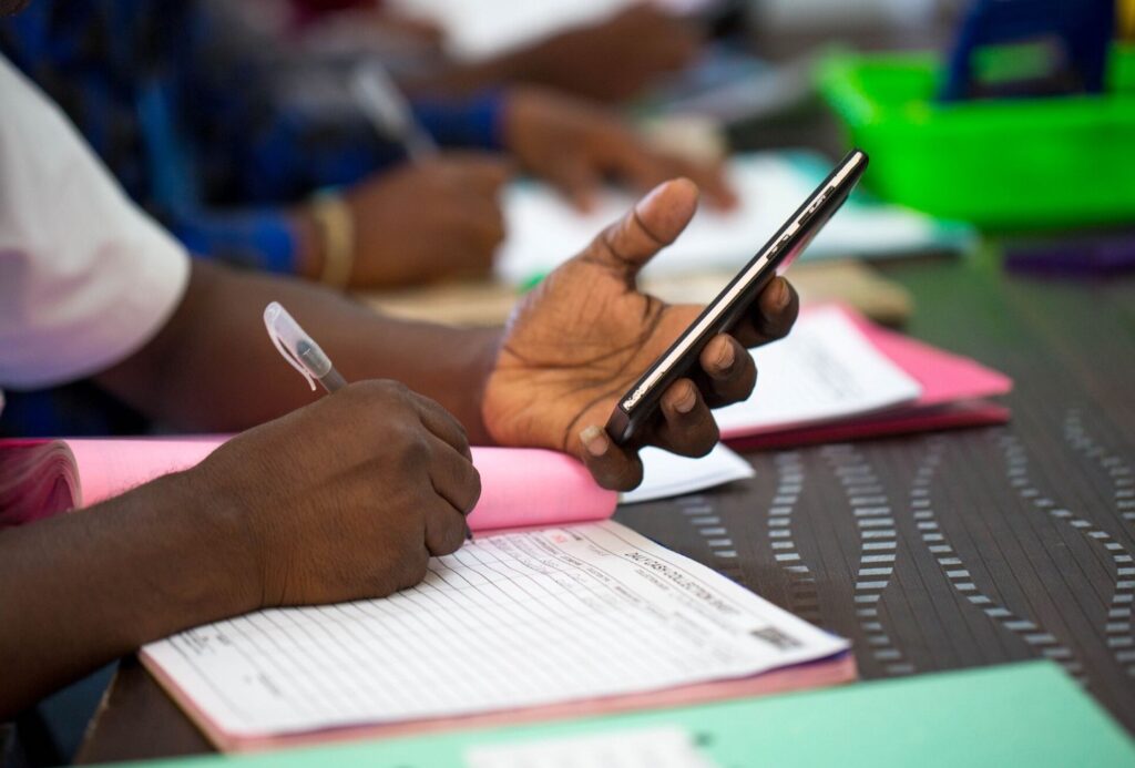 Person filling out paperwork while using a smartphone