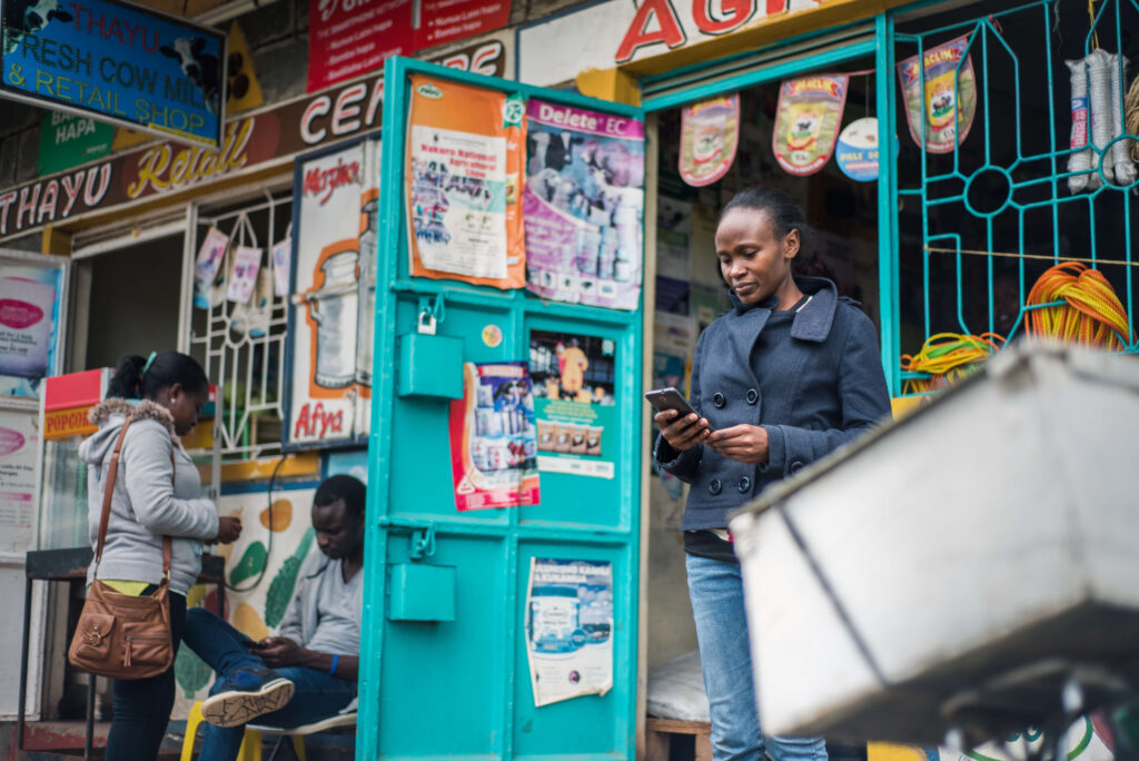 A woman scans her phone outside of a small agriculture sppuly store in Kenya