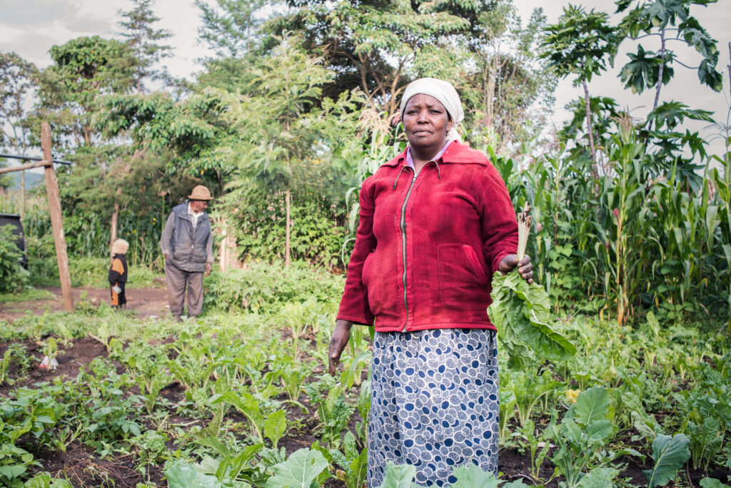 Farmer Virginia stands in field holding harvested vegetables