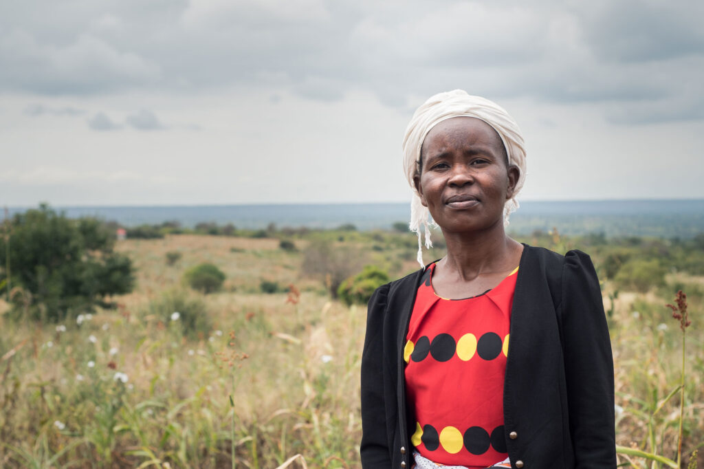 Rose stands smiling in a field in Kitui, Kenya