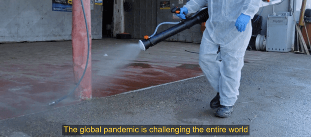 Open Opportunity COVID-19 response video screenshot. In the frame, a sanitation worker is spraying the streets. Caption reads, "The global pandemic is challenging the entire world."