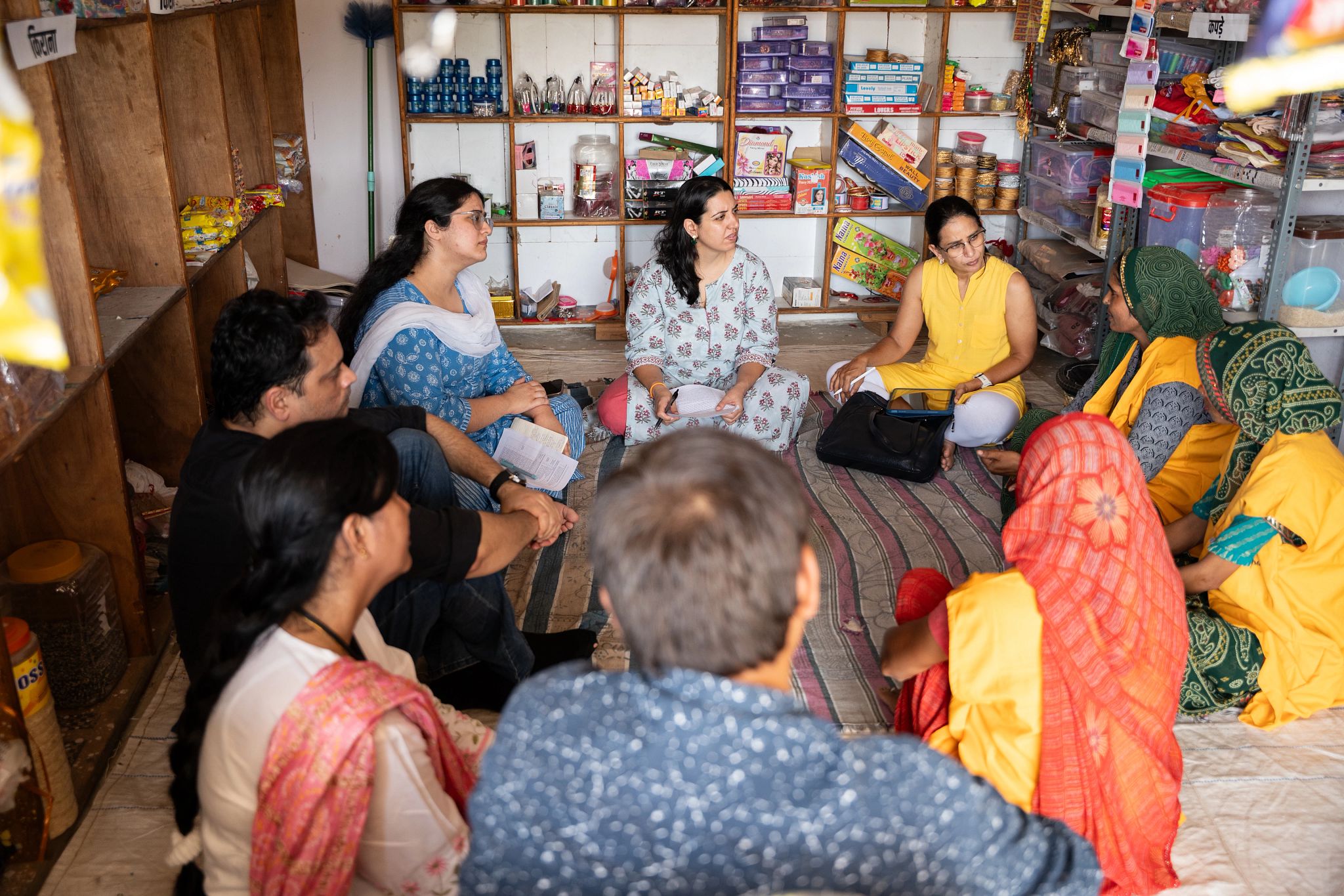 Frontier Markets and Accion Advisory team members sit with rural women entrepreneurs inside a village shop, discussing business challenges and training needs.