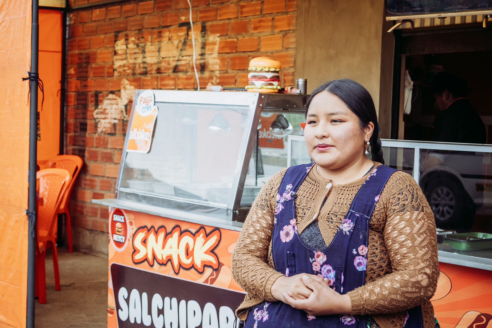 A lady standing in front of her salchipapas/snack store